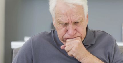 Mature man sitting on sofa coughing at his home
