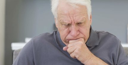Mature man sitting on sofa coughing at his home