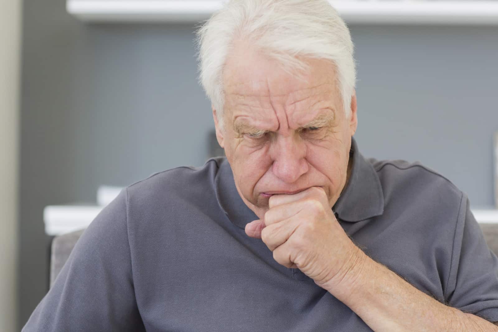 Mature man sitting on sofa coughing at his home
